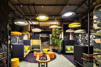 Modern lounge met blauwe en groene fauteuils, gele en oranje poefs, hangende design-lampen in geel en wit, zwarte muren met p