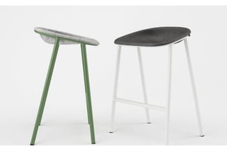 Twee barkrukken met ovale zitting: links groen metalen frame met grijze stof, rechts wit metaal met zwarte zitting.