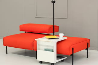 Rode modulaire zitbanken met zwarte metalen poten, witte bijzettafel op wielen met boeken en koffiemok, zwarte staande lamp i