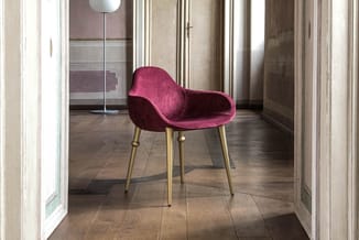 Bordeauxrode fluwelen stoel met armsteunen en goudkleurige metalen poten in modern interieur met houten vloer.
