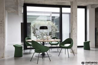 Moderne vergaderruimte met ronde tafel, groene stoelen met zwarte poten, zwarte hanglamp en betonnen kolommen. Grote ramen en