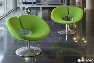 Twee lime groene designstoelen met organische vorm en metalen voet in moderne kantoorhal met donker tegelvloer.