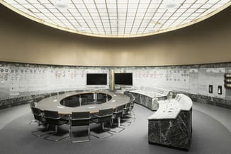 Moderne ronde vergadertafel met zwarte stoelen in circulaire opstelling, marmeren wandbekleding, grote schermen, gridplafond
