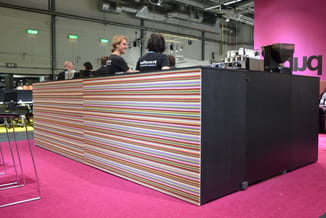 Baliebanktoestel met gekleurde horizontale strepen op roze vloer in industriële ruimte met medewerkers.