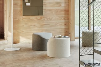 Houten interieur met twee ronde poefjes in beige en grijs, boek op zitting, metalen deurkozijn rechtsvoor.