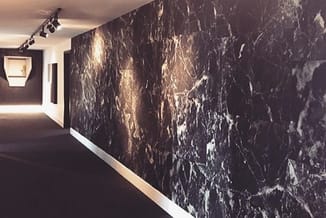 Moderne gang met zwarte marmeren wand met goudkleurige aders, witte plint, spotlighting en gesloten deur.