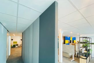 Modern kantoor met grijze akoestische scheidingswand, witte plafondpanelen, houten vloer, zithoeken met gele accenten en blau