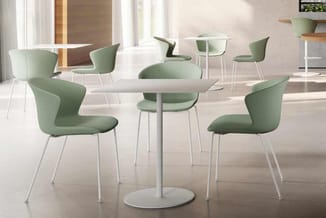Moderne vergaderruimte met ronde witte tafel, groengestoffeerde stoelen met metalen poten en hoge ramen met natuurlijk licht.