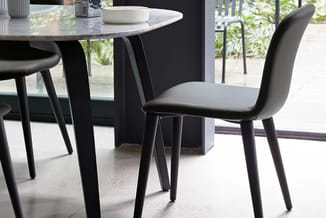 Ronde tafel met zwart onderstel en grijze blad, zwarte stoelen met grijze zitting in moderne kantoorruimte met glazen wand.