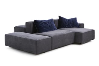 Grijze modulaire bank met donkerblauwe fluwelen kussens, lage zithoeken en uitnodigende zitvlakken.