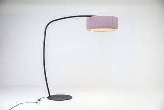 BuzziJet vloerlamp met een zwart gebogen frame, ronde voet en lichtroze cilindervormige kap tegen een witte achtergrond.