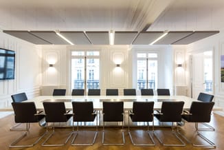 Moderne vergaderruimte met witte wandpanelen, lange witte tafel en zwarte kantooorstoelen met chromen onderstel, raampartijen