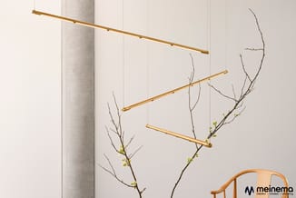 Hangende gouden stangen met tak-decoratie en kleine groene bloemen tegen witte wand met betonnen pilaar.