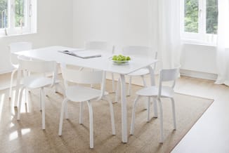 Witte vergadertafel met zes witte stoelen rond een beige vloerkleed in een lichte kantoorruimte met grote ramen.