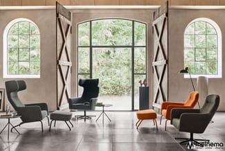 Moderne lounge met grijze en oranje fauteuils, poef, zwarte tafels, grote ramen met openslaande deuren en groene uitzicht.