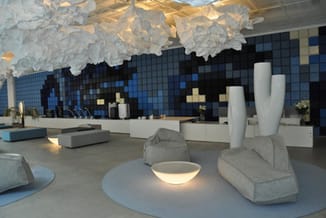 Moderne kantoorruimte met grijze betonnen zitblokken, witte vaazen, hangende witte sculpturen, blauwe gePixeleerde wandtegels