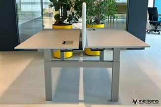 Moderne vergadertafel met licht houten blad en grijs metalen onderstel in heldere kantoorruimte met gele plantenpotten en gla