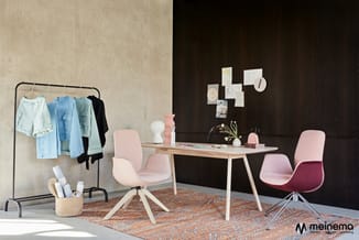 Kantoor inrichting met licht houten bureau, roze stoelen, kledingrek met blauwe en zwarte kledingstukken, en bruinoranje vloe