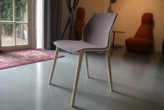 Grijze stoel met houten poten in moderne kantoorruimte met oranje muur, houten deunen en rode vloerkleed.