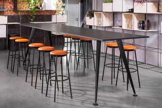 Lange vergadertafel met zwart blad en zwarte poten, omgeven door tien barkrukken met oranje zittingen in modern kantoorinteri