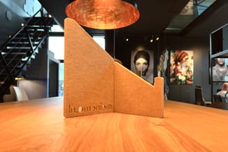Goudkleurige houten akoestische scheidingswand met opschrift "In.omeniom" op houten tafel in modern kantoor met koperen hangl