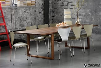 Houten vergadertafel met beige en witte kunststof stoelen met metalen poten in industriële ruimte met betonnen muur.