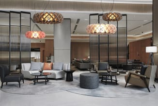 Lounge-interieur met vier Halo hanglampen in bruin, roze en licht vilt boven een zithoek.