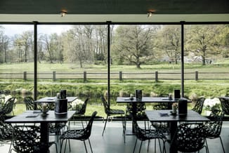 Moderne vergadertafels met zwarte metalen onderstel en zwarte design stoelen in glazen paviljoen met uitzicht op park en wate
