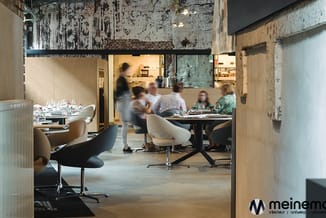 Moderne kantoorruimte met beige draaistoelen, zwarte ronde vergadertafel, houten wanden en grijs betonplafond. Medewerkers aa