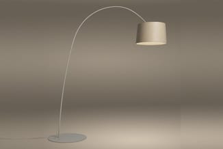 Booglamp met beige linnentapijt kap, wit metalen boog en ronde voetplaat in minimalistisch interieur.