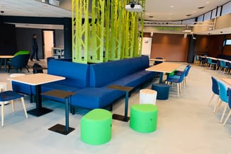 Modern kantoor met blauwe hoekbank, groene poef-zitjes, houten tafels, blauwe stoelen en geel-groene akoestische scheidingswa