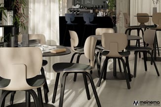 Modern café-interieur met crèmekleurige stoelen met zwart frame, zwarte tafels, groenplanten, en een zwarte balie op de achte