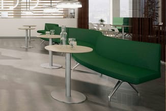 Moderne kantoorruimte met groene loungebanken, ronde houten tafels op zilveren poten, glazen waterkannen en staande tafels in