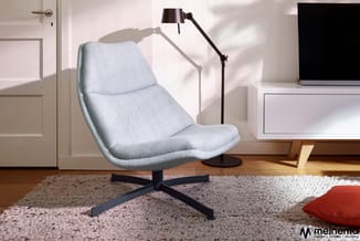 Lichtblauwe loungestoel met zwart kruisvormig onderstel op tapijt, naast zwarte vloerlamp en wit bureau in minimalistisch int