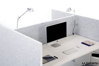 Compacte werkplek met grijze akoestische wanden, wit bureau, iMac-computer, bureau-lamp, toetsenbord en muis.
