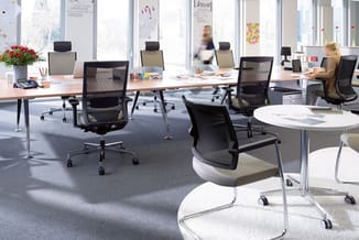 Modern kantoor met zwarte mesh ergonomische bureaustoelen, houten en witte werkplekken, ronde vergadertafel, grote ramen, gri
