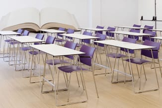 Vergaderruimte met rechthoekige tafels, paarse stapelstoelen met zilveren frames en groot opengeslagen boek als wanddecoratie