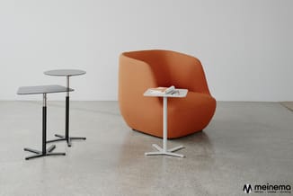 Oranje ronde fauteuil met witte bijzettafel en zwarte staande tafel met grijs blad in minimalistisch interieur.