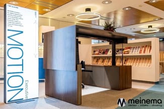 Moderne receptie met houten bureau, witte kasten met magazines, blauwe MOTION-banner, grijze scheidingswanden en verlichte pl