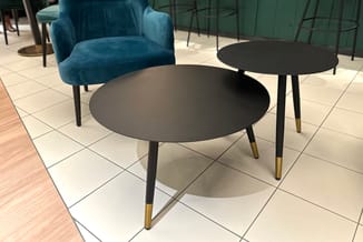 Lounge-opstelling met blauwe fauteuil en twee zwarte ronde tafels met zwarte poten en goudkleurige accenten op lichte tegelvl