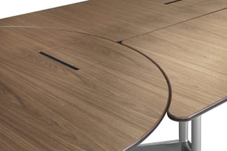 Houten vergadertafel met organische vorm, bruin fineer, zilverkleurig metalen onderstel, kabelgaten zichtbaar.