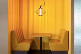 Twee gele stoelen met strepenpatroon aan tafel in geel ingerichte nis met hangend geometrisch lampje.