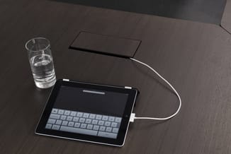 iPad op donkerbruine houten tafel met toetsenbord, glas water en zwart notitieblok, werkplek opstelling.