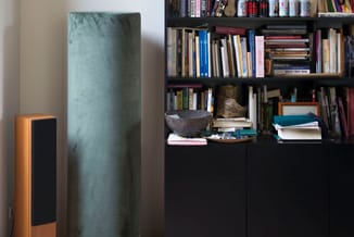 Interieurimpressie met zwarte boekenkast, grijsgroen akoestisch paneel, houten speaker en decoratieve objecten op zwarte kast