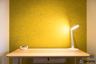 Houten bureau met witte LED-bureaulamp en witte kom met inhoud tegen gele achtergrond in kantoorruimte.