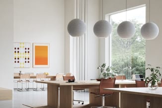 Modern kantoor met houten bureaus, bruine bureaustoel, grijze bolhanglamp, kleurrijke wandkunst en groene planten bij groot r