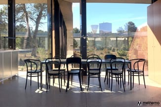 Zwarte stoelen rond grijze tafel in modern kantoor met glazen wand, uitzicht op natuur en gebouwen.