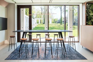 Moderne vergaderruimte met zwarte bartafel, bruinleren barkrukken, blauwe tapijt, grote raampartijen naar tuin, TV-scherm lin