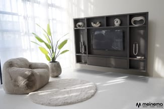 Moderne woonkamer met grijze boucléstoel, wollen vloerkleed, potplant en zwart TV-kastensysteem met decoratieve objecten tege