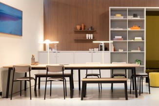 Kantoorruimte met lange houten tafel, zwarte stoelen, witte kastenwand, grijze open kastjes, houten wandpanelen en verlichtin